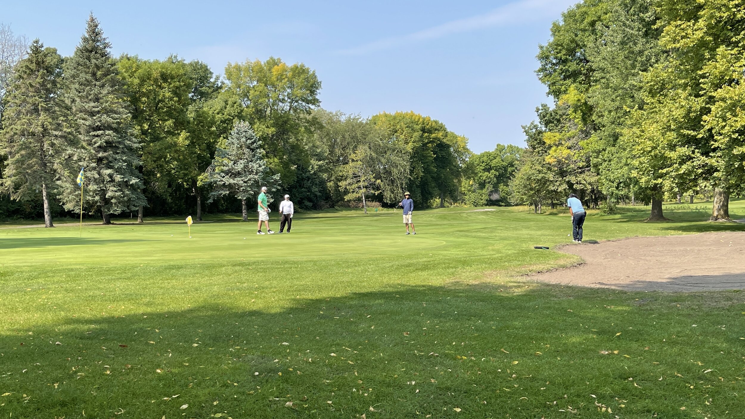 Four golfers on and around a tree-lined green beside a sand bunker at Montgomery National Golf Club