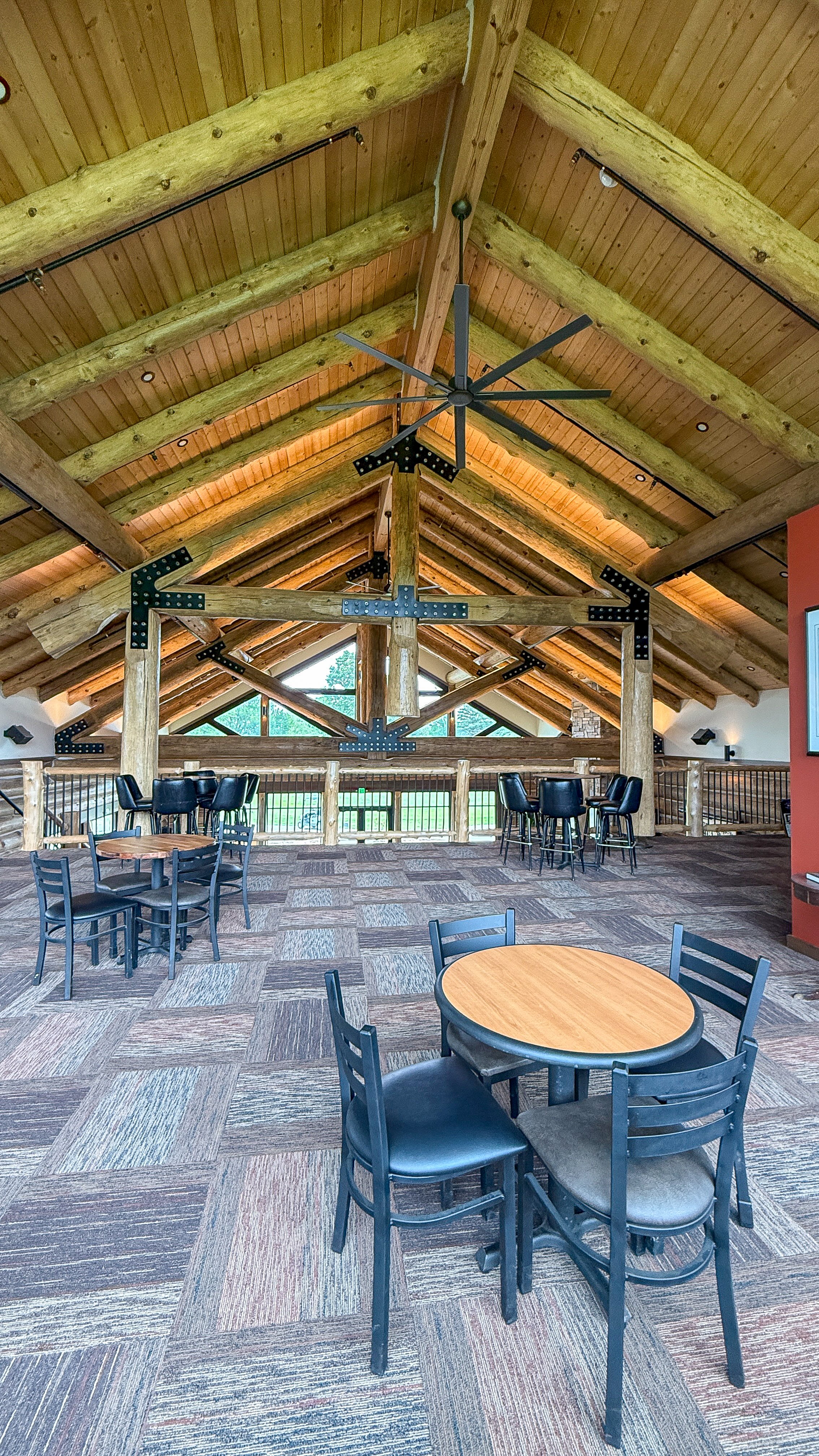 Tables and chairs on the upper level under a vaulted log ceiling