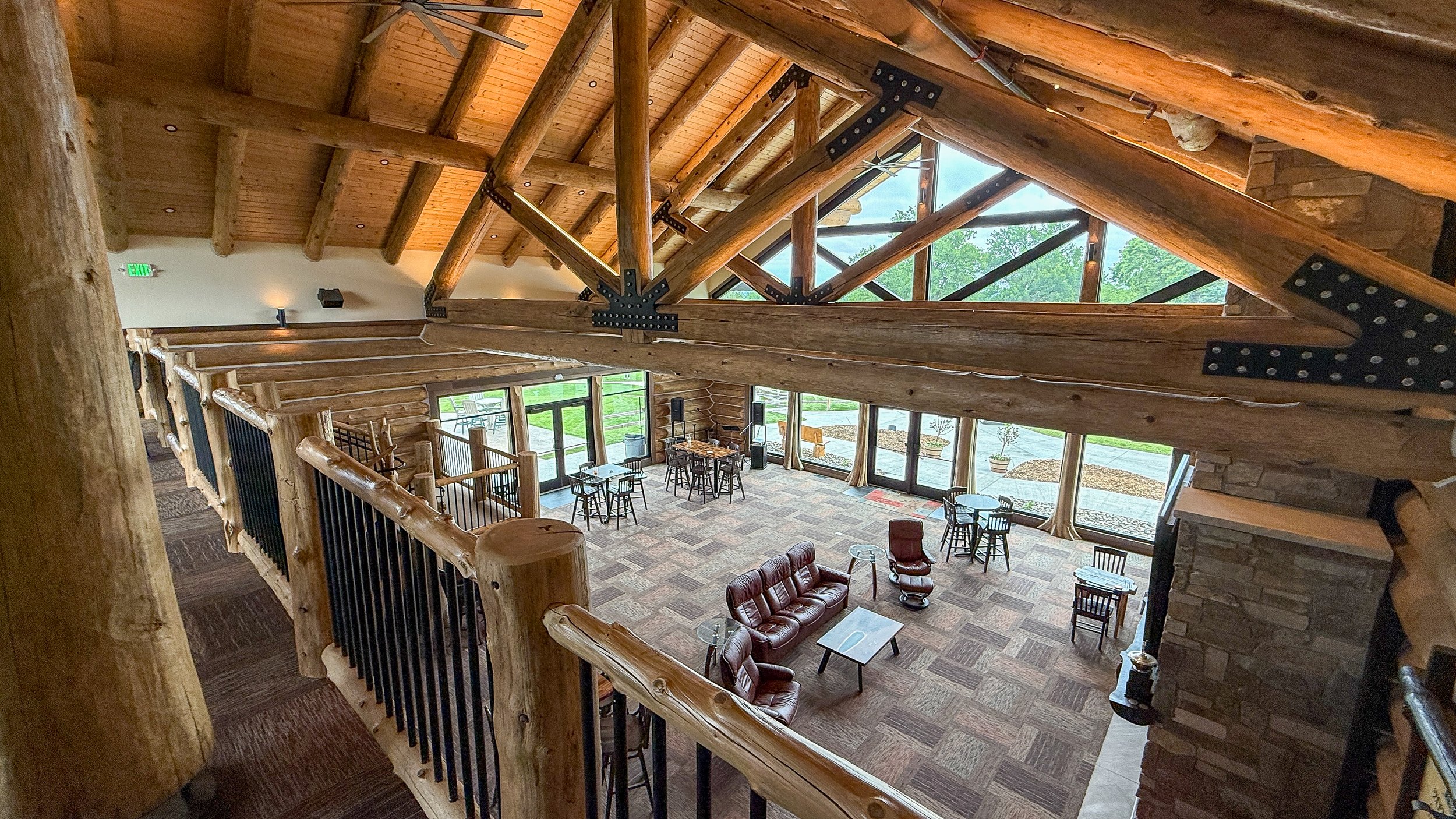 View from the upper-level railing down into the Montgomery National clubhouse, with log trusses, tall windows and lounge seating