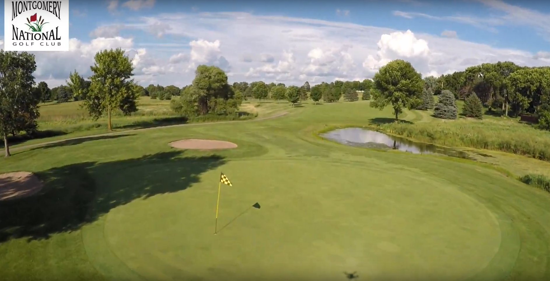 Drone view of a flagged green with a sand bunker and a pond beyond at Montgomery National