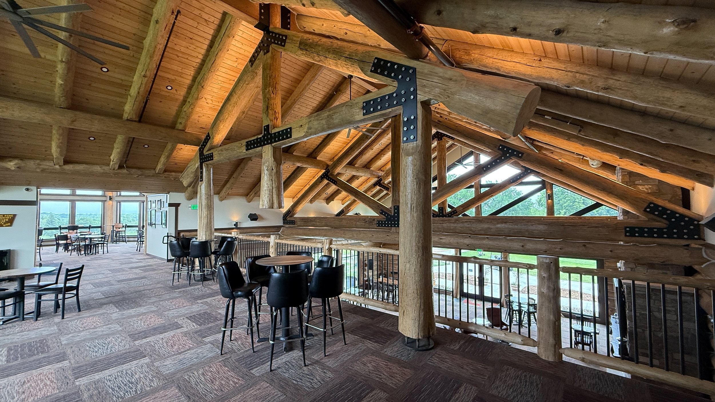High-top tables along the upper-level railing beneath the timber trusses