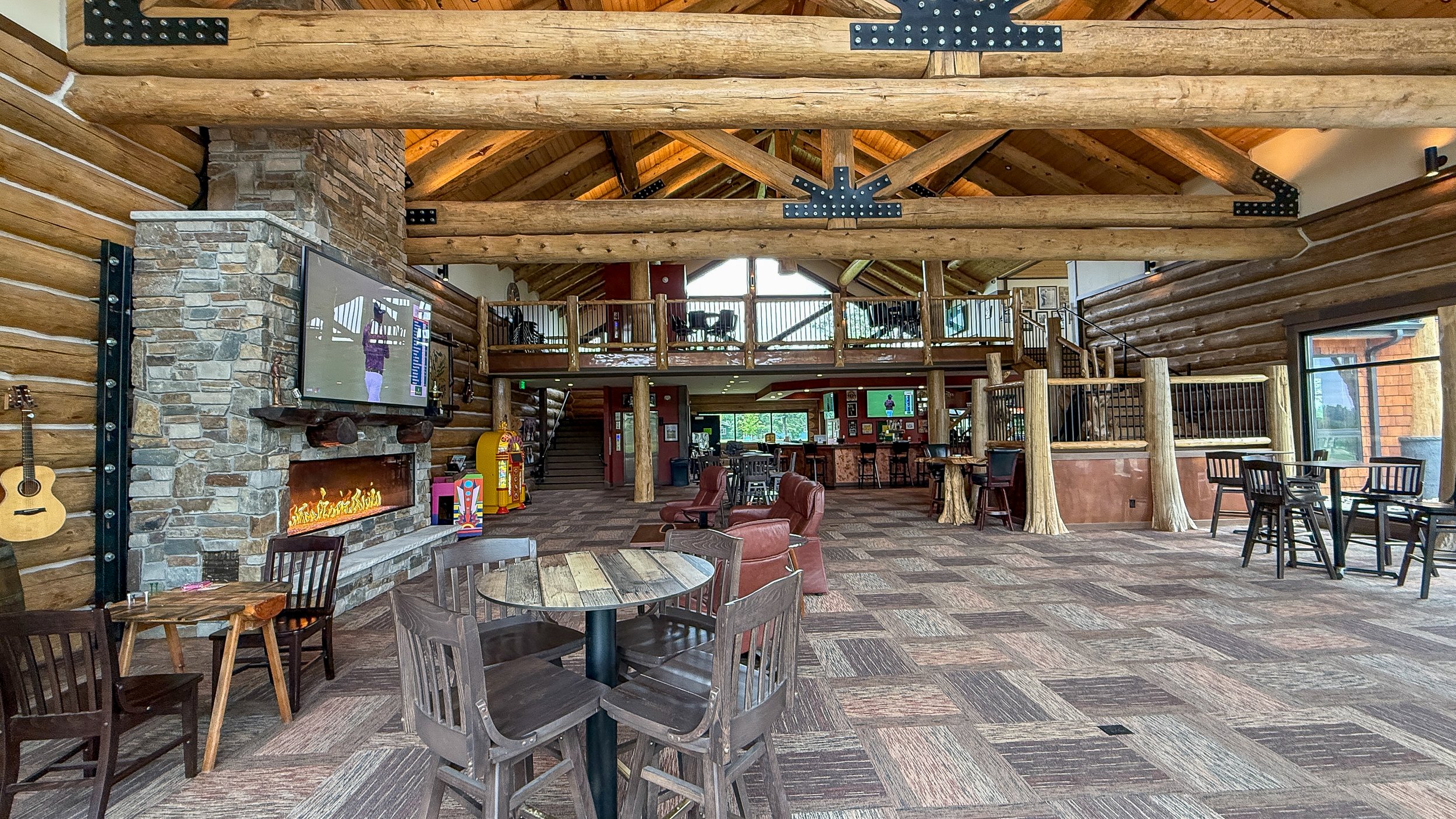 Stone fireplace, bar-height tables and the loft balcony in the log cabin clubhouse great room at Montgomery National