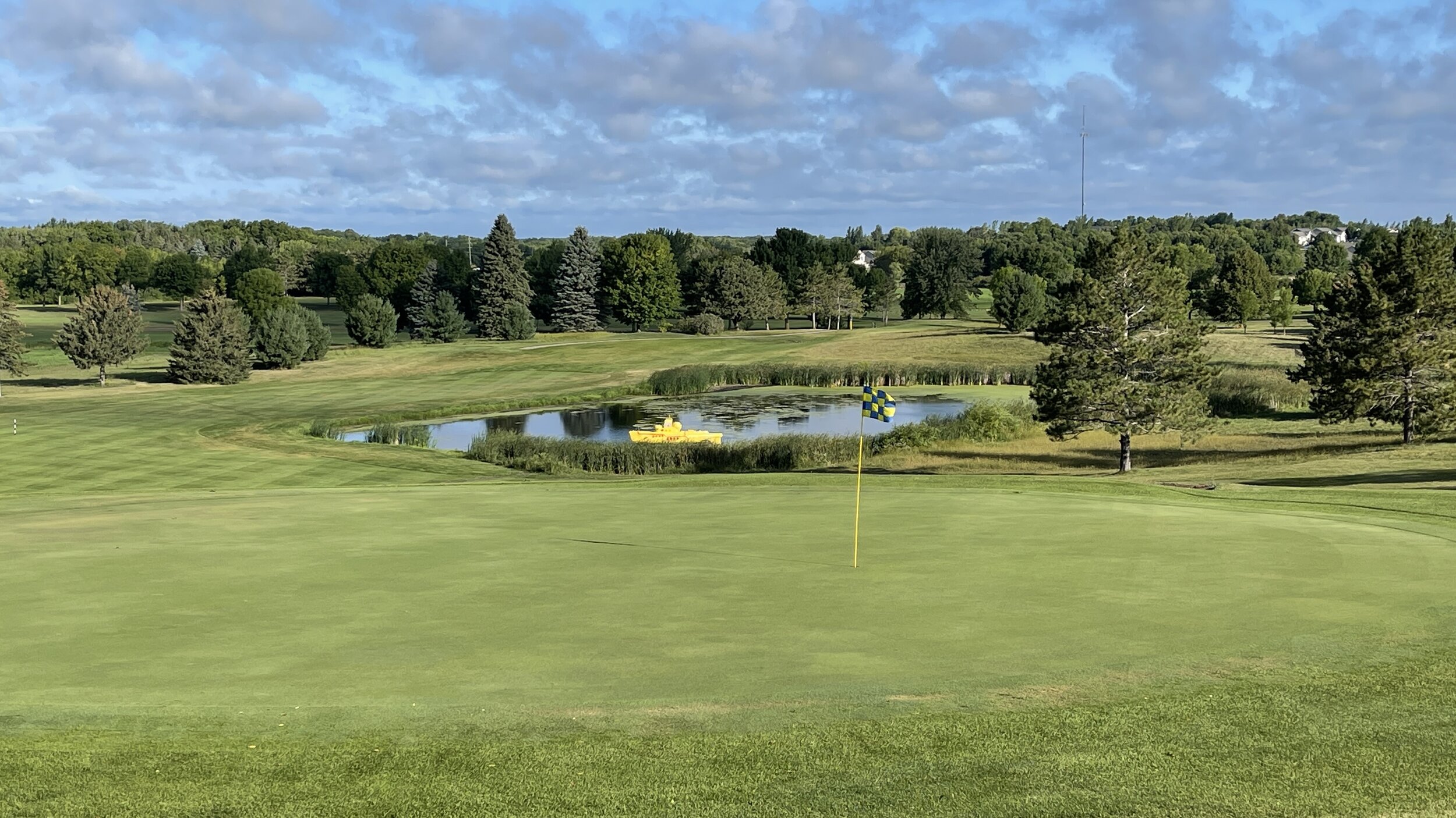 A green and flagstick in front of the pond with the yellow submarine at Montgomery National